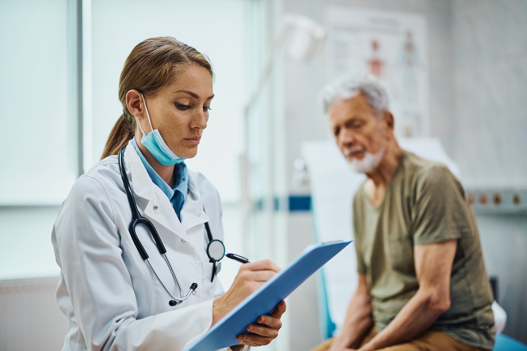 Female doctor writing data in senior patient's medical record after examination at the clinic.